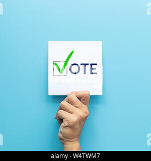 hand holding white paper with the 'vote' and green check mark voting symbols in checkbox of the inscription isolated on blue background Stock Photo