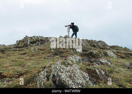 Young tourist woman looking through coin operated high powered binoculars on the Caucasus Mountains, Kazbegi, Georgia Stock Photo