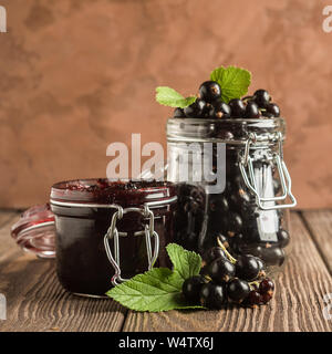 Jam and fresh black currant berries in glass jars stand on a wooden background. Square frame Stock Photo