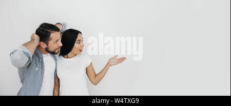 Pretty couple, man and woman emotionally advertising product pointing hand on empty background. Stock Photo