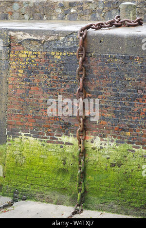 Large rusty old fishing boat chain hanging down the wet harbour (harbor) wall. Stock Photo