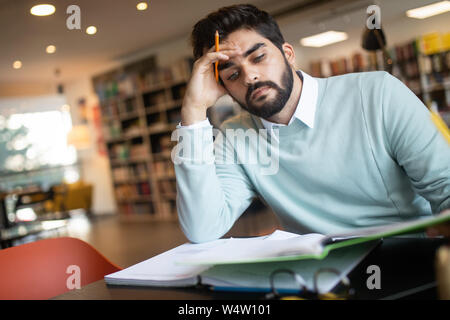 Exhausted young man student studying in a library Stock Photo