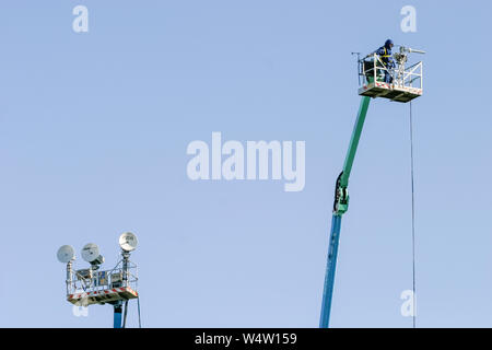 Cameraman in a camera platform on top of a BBC Television Outside Broadcast crane or tower, next to a tower with satellite transmission dishes. Stock Photo