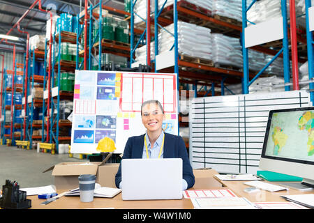 Female manager using laptop at desk in warehouse Stock Photo