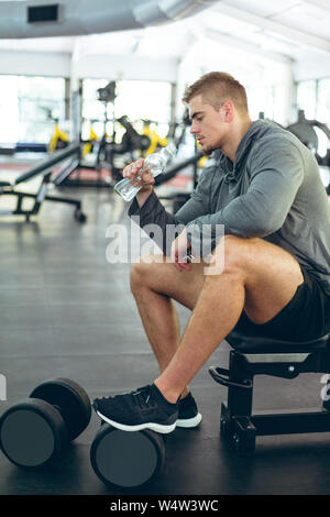 Male athletic drinking water while relaxing on bench in fitness center Stock Photo