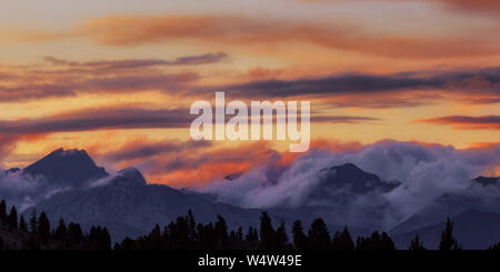 Wide angle panorama silhouette forest and mountain tops in red orange blue clouds gradient sunset. Stock Photo