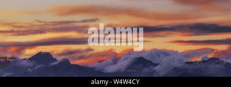 Wide angle panorama silhouette forest and mountain tops in red orange blue clouds gradient sunset. Stock Photo