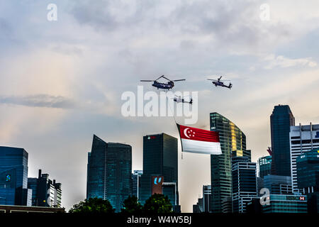 Singapore - Jul 14, 2018: Chinook flying a giant Singapore flag escorted by two Apache helicopter over Marina Bay as part of Singapore National Day Pa Stock Photo