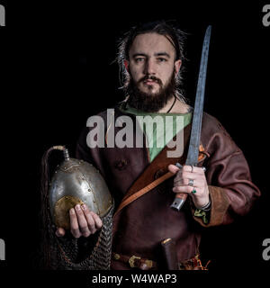 Slavic bearded warrior dressed in leather armor of the Viking Age holding a sword and helmet. Allegory of Power, Protection, Security Stock Photo