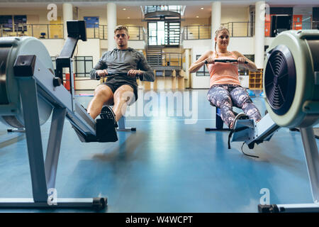 Male and female athlete exercising with rowing machine in fitness studio Stock Photo