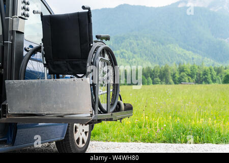 Black electric lift specialized vehicle for people with disabilities. Empty wheelchair on a ramp with nature and mountains in the back Stock Photo