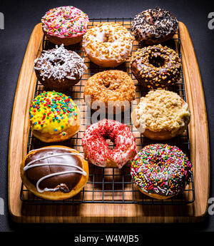 assorted donuts on wire rack on wooden cutting board Stock Photo