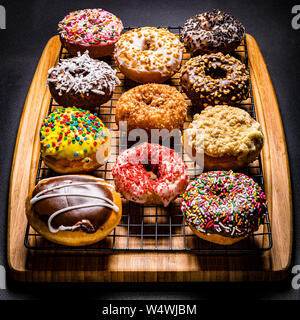 assorted donuts on wire rack on wooden cutting board Stock Photo