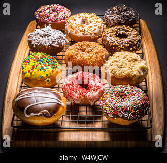assorted donuts on wire rack on wooden cutting board Stock Photo