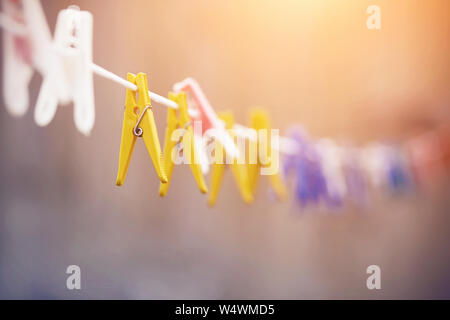 Many plastic clothespins of different colors - white, yellow, blue and others hang on a white clothesline and are illuminated by light. Stock Photo