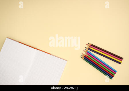 Open notebook and color pencils on yellow background Stock Photo