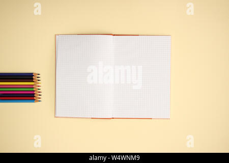 Open notebook and color pencils on yellow background Stock Photo