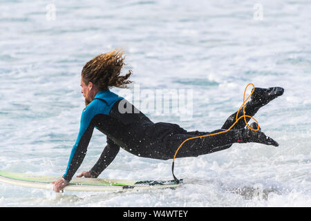 A male surfer launching himself and his surfboard into the sea at Fistral in Newquay in Cornwall.