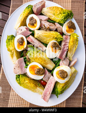 Version of salad Nicoise on white plate.  Hard boiled eggs and olive dressing, baby gem lettuce, boiled potatoes & tuna steak slices Stock Photo