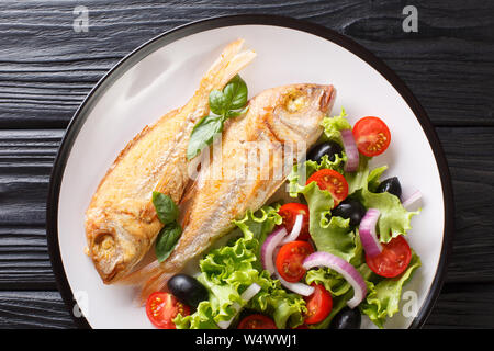 Tasty fried pink dorado or gilt-head bream fish with vegetable salad close-up on a plate on the table. Horizontal top view from above Stock Photo