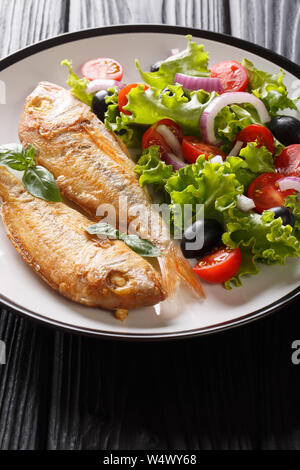 Tasty fried pink dorado or gilt-head bream fish with vegetable salad close-up on a plate on the table. vertical Stock Photo