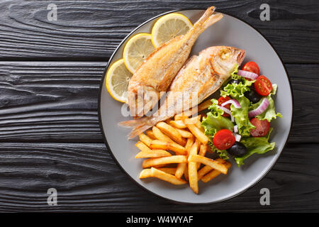 Portion of fried pink dorado fish with french fries and vegetable salad closeup on a plate on the table. horizontal top view from above Stock Photo