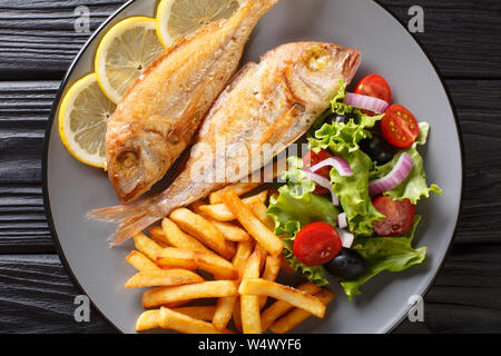 Freshly made pink dorado fish with french fries, lemon and vegetable salad close-up on a plate on the table. Horizontal top view from above Stock Photo