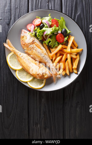 Portion of fried pink dorado fish with french fries and vegetable salad closeup on a plate on the table. Vertical top view from above Stock Photo