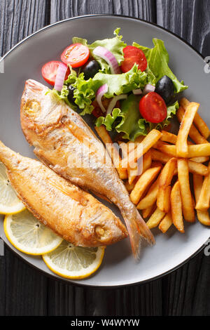 Freshly made pink dorado fish with french fries, lemon and vegetable salad close-up on a plate on the table. Vertical top view from above Stock Photo