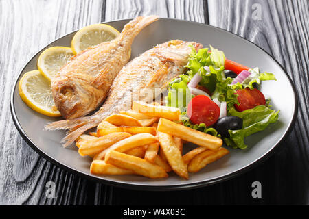 Fish menu fried pink dorado with french fries, lemon and vegetable salad close-up on a plate on the table. horizontal Stock Photo