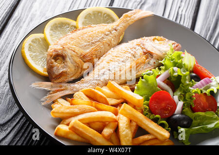 Freshly made pink dorado fish with french fries, lemon and vegetable salad close-up on a plate on the table. horizontal Stock Photo
