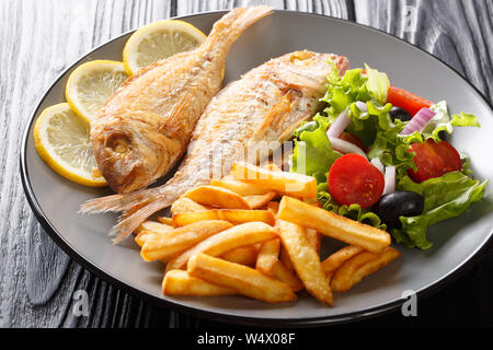 Portion of fried pink dorado fish with french fries and vegetable salad closeup on a plate on the table. horizontal Stock Photo