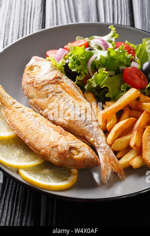 Tasty fried pink dorado or gilt-head bream fish with french fries and vegetable salad close-up on a plate on the table. vertical Stock Photo