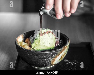 Hand pouring chocolate syrop on pistachio ice cream in a black bowl with blurred background Stock Photo