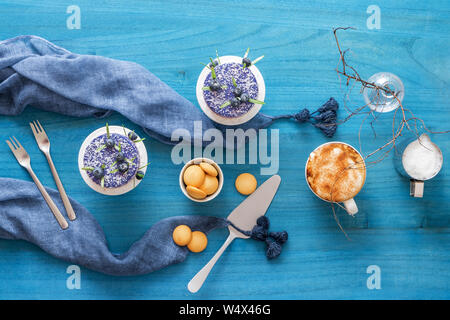 Two round no bake blueberry mini cheesecakes enveloped in coconut and embellished with real blueberries and rosemary leaves. Blue wooden table with co Stock Photo