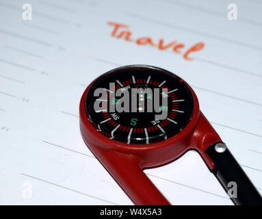 A close-up shot showing the right edge of a small red plastic compass resting on a white lined planner page, with the word "Travel" Stock Photo
