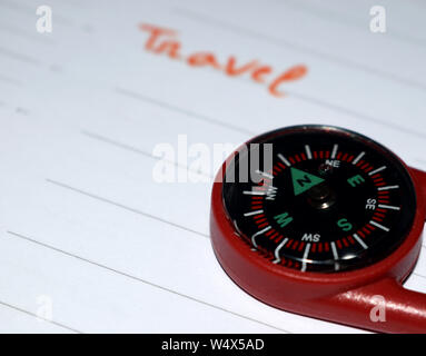 A close-up shot showing the right edge of a small red plastic compass resting on a white lined planner page, with the word "Travel" Stock Photo