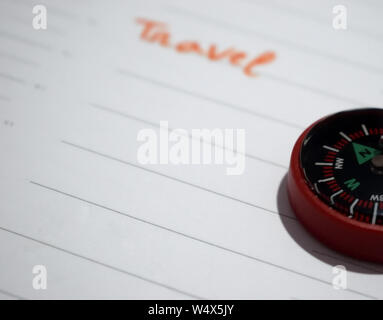 A close-up shot showing the right edge of a small red plastic compass resting on a white lined planner page, with the word "Travel" Stock Photo