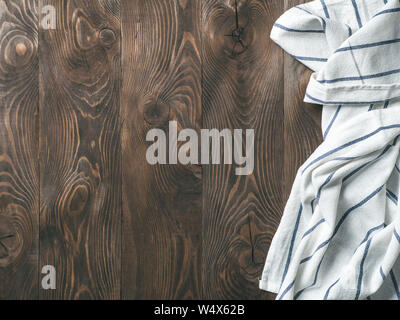 View from above on brown wooden table with linen kitchen towel or textile napkin. Blue tablecloth on dark brown wood tabletop. Copy space for text. Ca Stock Photo