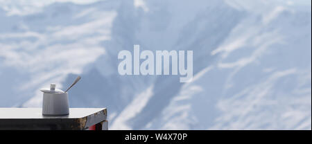 Old table with sugar bowl in outdoor cafe at ski resort and snowy sunlight mountains at background. Panoramic view. Stock Photo