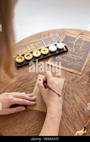 A calligrapher woman is holding a pen with ink in front of an empty postcard before starting work. Soft focus Stock Photo