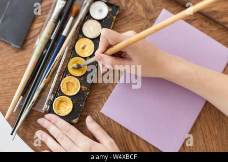 The artist is preparing to work. Applies paint to the brush. Close-up. The atmosphere of the creative workshop Stock Photo
