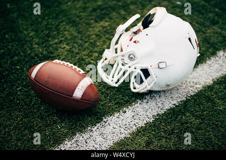 Photo of white helmet of Amerinian football player and ball on green lawn Stock Photo