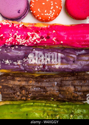 Eclairs, macarons, French pastry glazed Eclairs with nuts, berry cream and chocolate. Gentle color macaroons . Variety Selection. top view Stock Photo