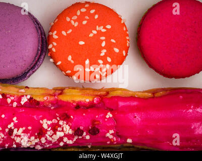 Eclairs, macarons, French pastry glazed Eclairs with nuts, berry cream and chocolate. Gentle color macaroons . Variety Selection. top view Stock Photo