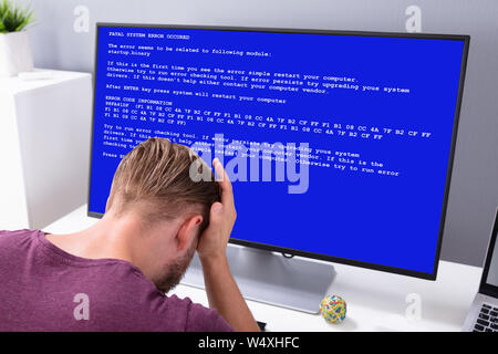 Worried Man At Computer With System Failure Screen At The Workplace Stock Photo