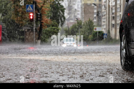Torrential rain at crossroads and red light reflected in the flow of water on a city street. Stock Photo