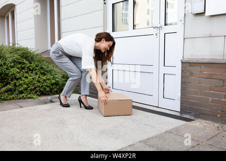 Smiling Young Woman Peeking Up The Delivered Parcel At The Door Entrance Stock Photo