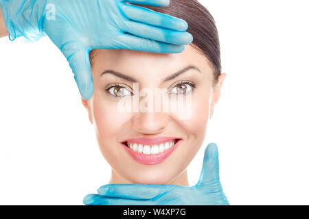 Aesthetic procedure. Doctor hand in gloves shaping a frame around face of a girl. Woman with plastic surgery isolated cutout on white background with Stock Photo