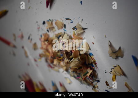 Multi-colored pencil shavings on a white/grey background with natural light shining through. Stock Photo